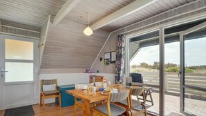 A cozy dining area with a wooden table and chairs, a hanging light fixture, and a view through large glass doors to the outside. - "Alleta" - 600m from the sea by Interhome (Ringkøbing)