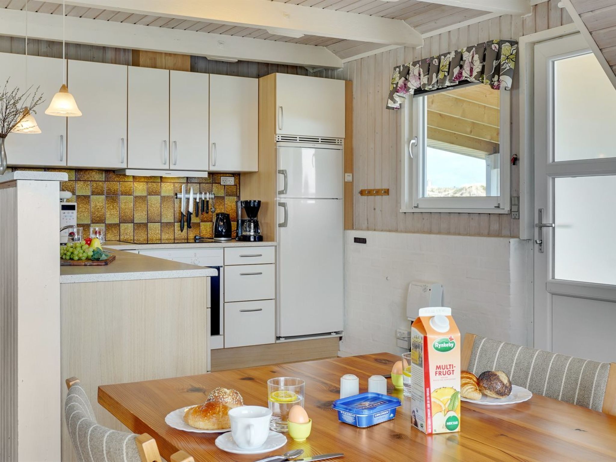 Eine moderne Küche mit weißen Schränken, einem Kühlschrank und einem Essbereich mit einem für das Frühstück gedecktem Tisch.
