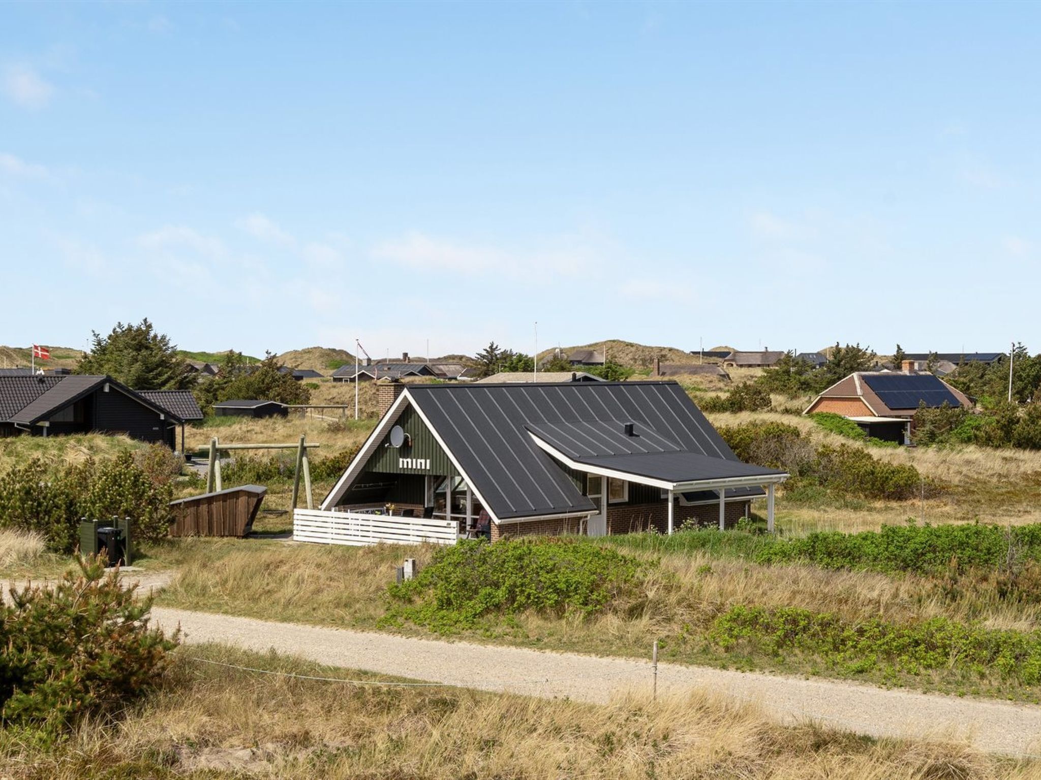 A modern house with a sloped roof and solar panels, surrounded by a rural landscape.