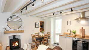 A cozy living room with a fireplace, a dining area, and a kitchen with modern appliances. - Bwthyn Lili (Cemaes Bay)