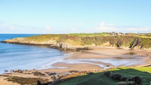 A coastal landscape with a sandy beach, grassy hills, and a clear blue sky. - Bwthyn Lili (Cemaes Bay)