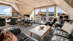 Un loft amplio con techo alto, vigas de madera, un ventanal grande y una zona de estar acogedora con sofás de cuero y una mesa de comedor.