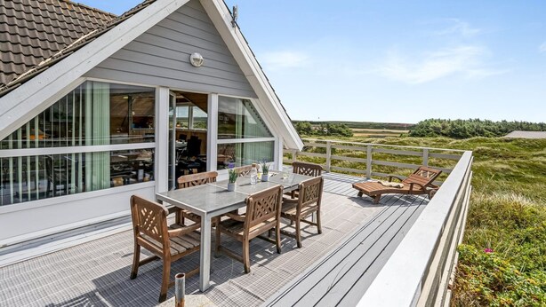 Una casa moderna con una amplia terraza, un comedor con mobiliario de madera y vistas al campo.