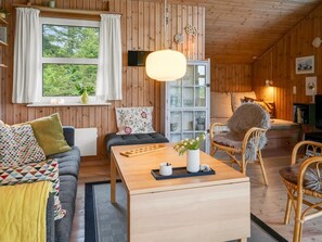 L’intérieur chaleureux d’un chalet, avec un décor en bois, un canapé, une table à manger, une chaise et une bibliothèque.