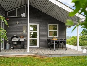 Une maison moderne dotée d’un porche abrité, d’un barbecue et d’un coin repas aménagé avec du mobilier d’extérieur.