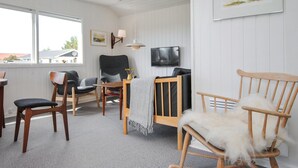 Ein gemütliches Wohnzimmer mit einem Schaukelstuhl aus Holz, einem grauen Sessel und einem Holztisch mit Fernseher.