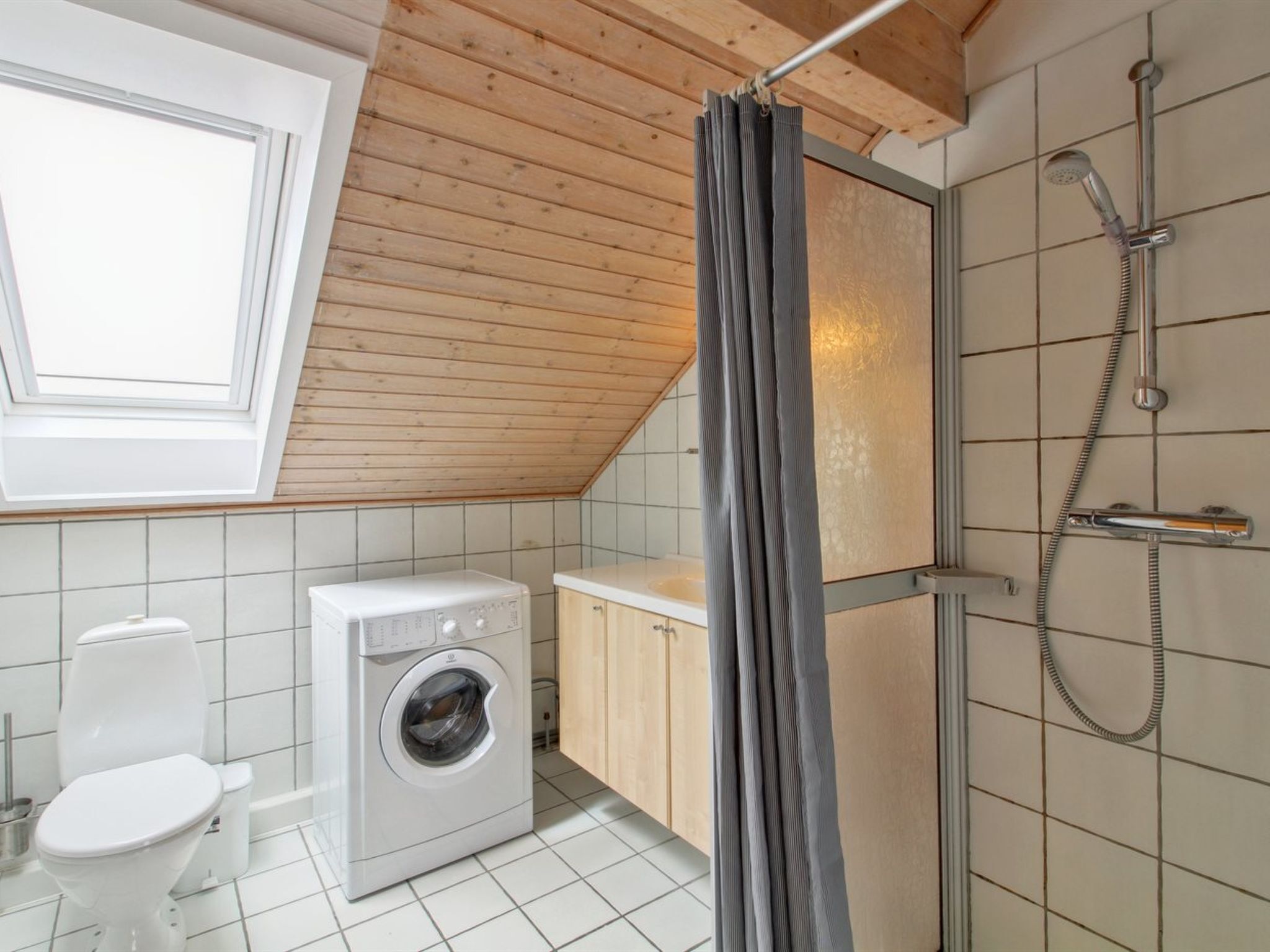 Ett litet badrum med tvättmaskin, toalett och dusch.