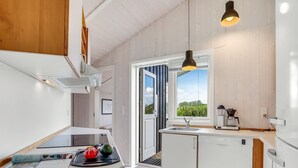 A modern kitchen with white cabinetry, a built-in dishwasher, and a window providing a view of greenery outside. - "Birtir" - 1.2km from the sea by Interhome (Væggerløse)