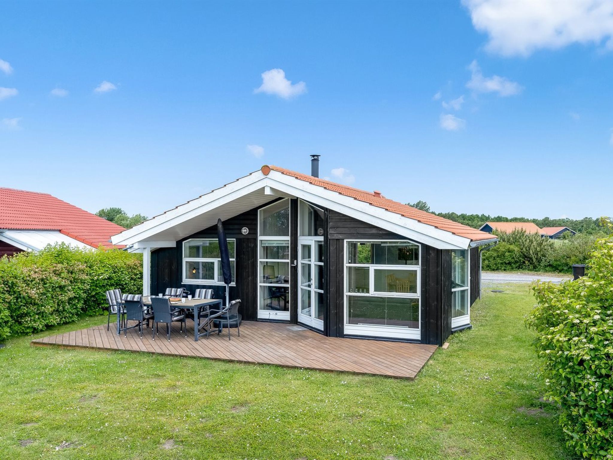A modern house with a deck, large windows, and a red roof.