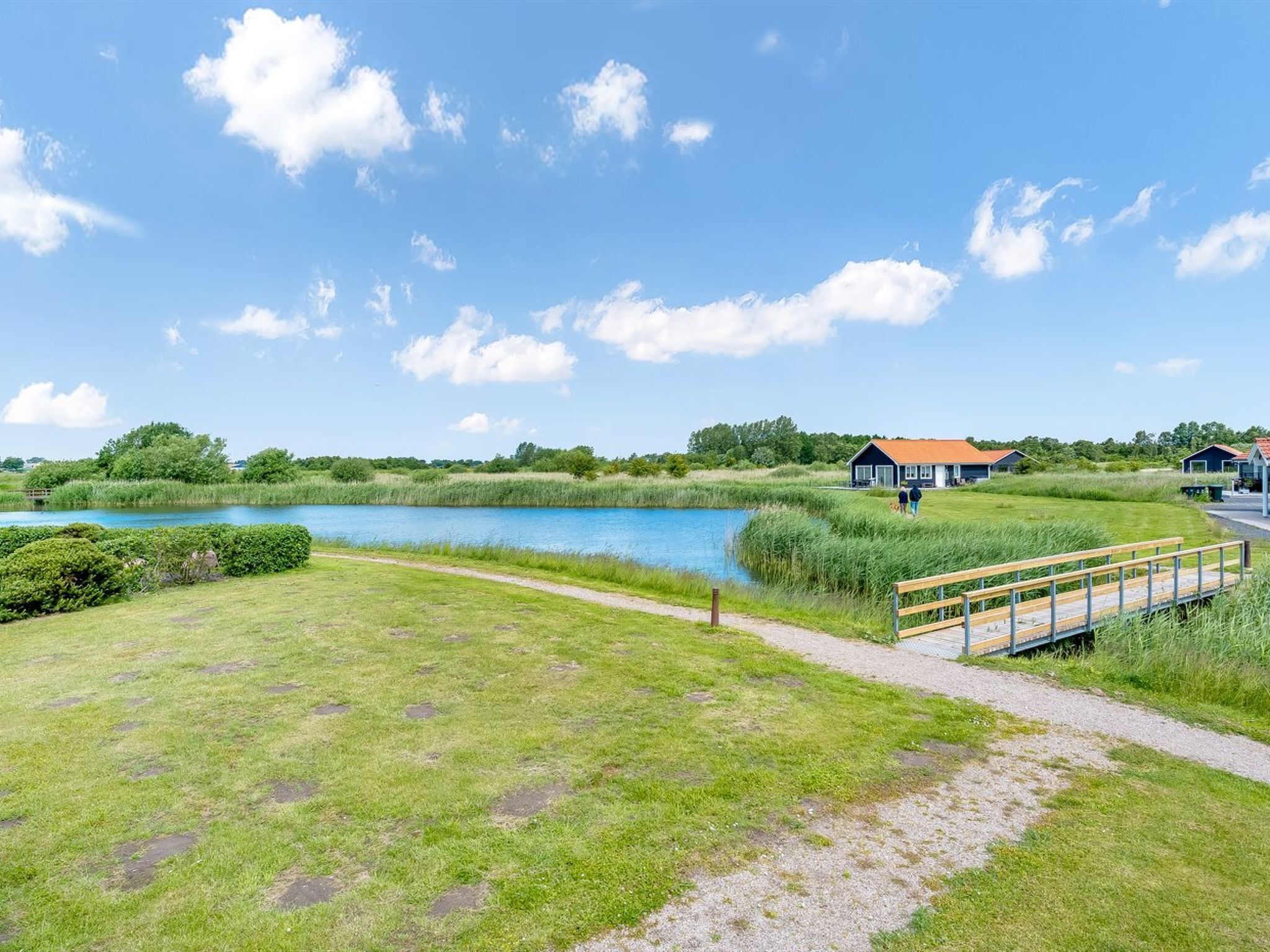 A lakeside property with a wooden bridge, a grassy area, and a building with a red roof.