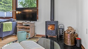 Un salon chaleureux avec un téléviseur, des meubles en bois, une cheminée et une vue sur les arbres à travers de grandes fenêtres.