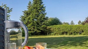 Une table dressée à l’extérieur, avec une carafe, des verres et un panier de nourriture.
