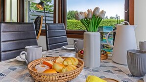 Une table mise pour le petit-déjeuner, avec un panier en osier rempli de viennoiseries, un vase de tulipes et une cafetière, le tout placé sur une table d’où l’on peut admirer la verdure environnante.