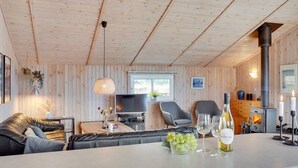 En mysig stuga med träpanel i taket, en soffa, en tv och en öppen spis.