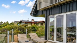 A modern house with a balcony featuring two lounge chairs and a glass door leading to a patio area.
