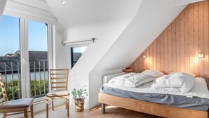 A modern bedroom with a sloped ceiling, a wooden bed frame, a large window, and a view of the outside.