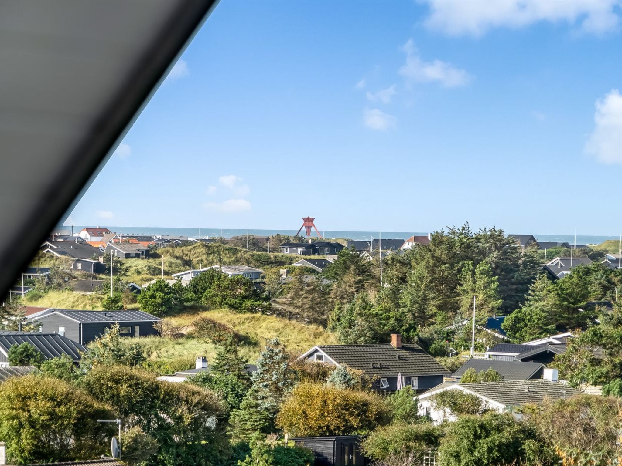 A residential area with houses, trees, and a view of the sea.