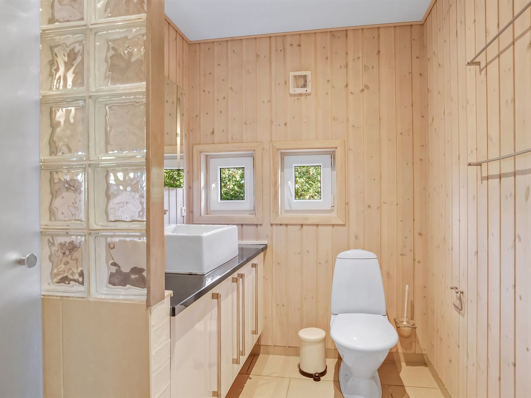A compact bathroom with wooden walls, a white toilet, and a small window.