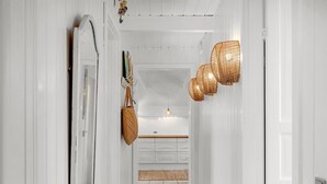 Een gang met witte muren, een spiegel, rieten manden en een hanglamp.