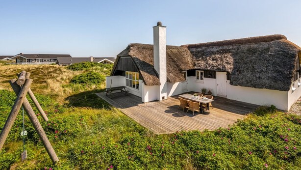 Een rieten huis met een houten terras en schoorsteen.