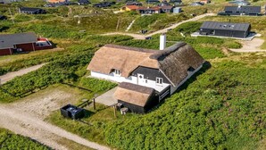 Een landhuis met rieten dak, omringd door een wijngaard, grenzend aan een grindpad.