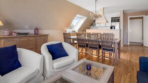 A modern living room with a glass coffee table, white sofas with blue cushions, a dining area with wooden chairs, and a kitchen in the background. - "Gerrit" - 450m from the sea by Interhome (Løkken)