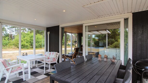 Een overdekt buitengebied met een houten tafel en stoelen, een barbecue en uitzicht op de omgeving.