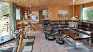 Een gezellig cabin interieur met een houten plafond, een eethoek met houten stoelen, een leren bank en een keuken op de achtergrond.