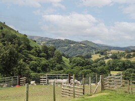 A rural landscape with rolling hills, a fenced area with sheep, and a clear sky.