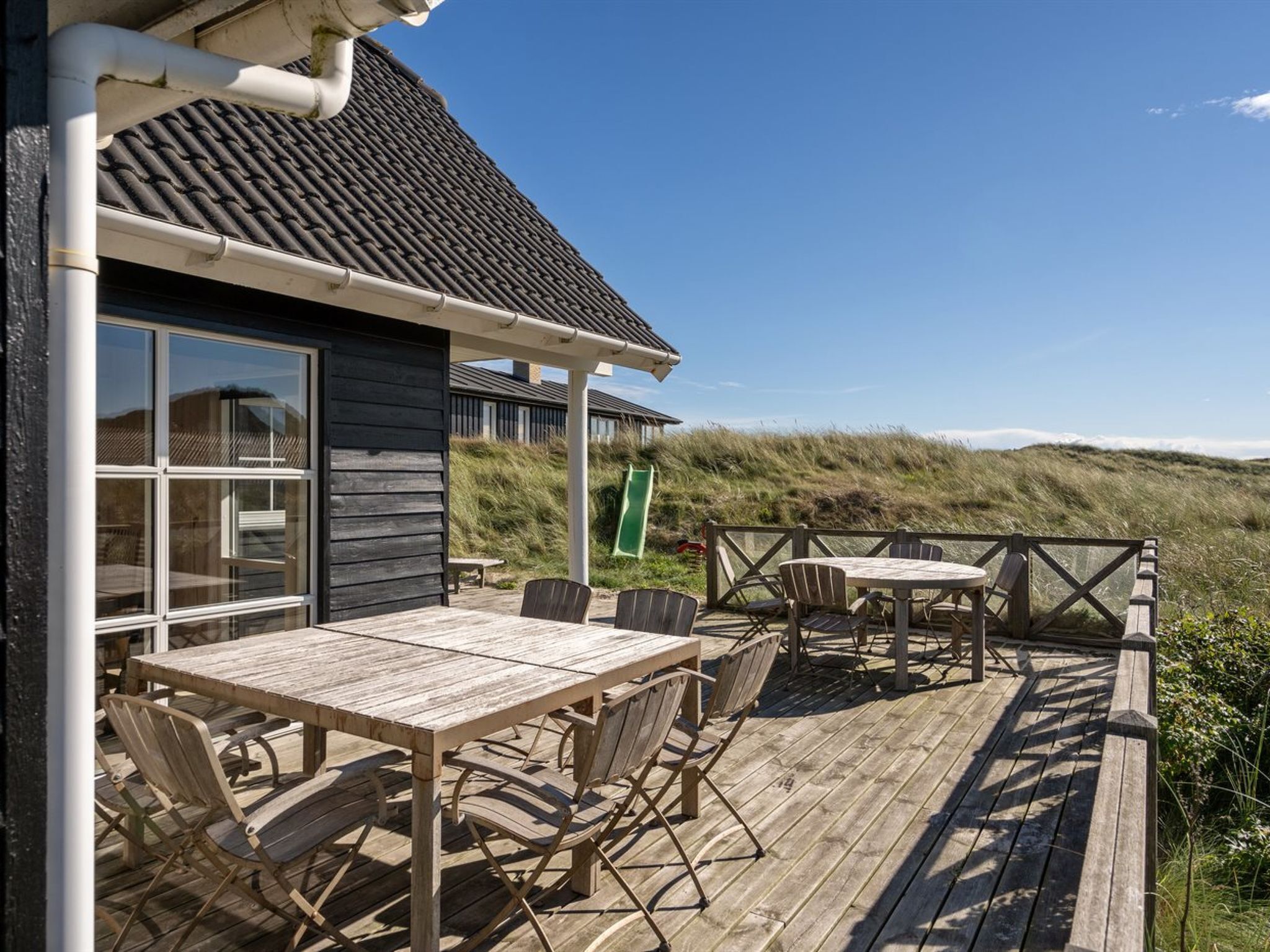 Une terrasse en bois avec une table et des chaises, donnant sur un paysage de dunes.