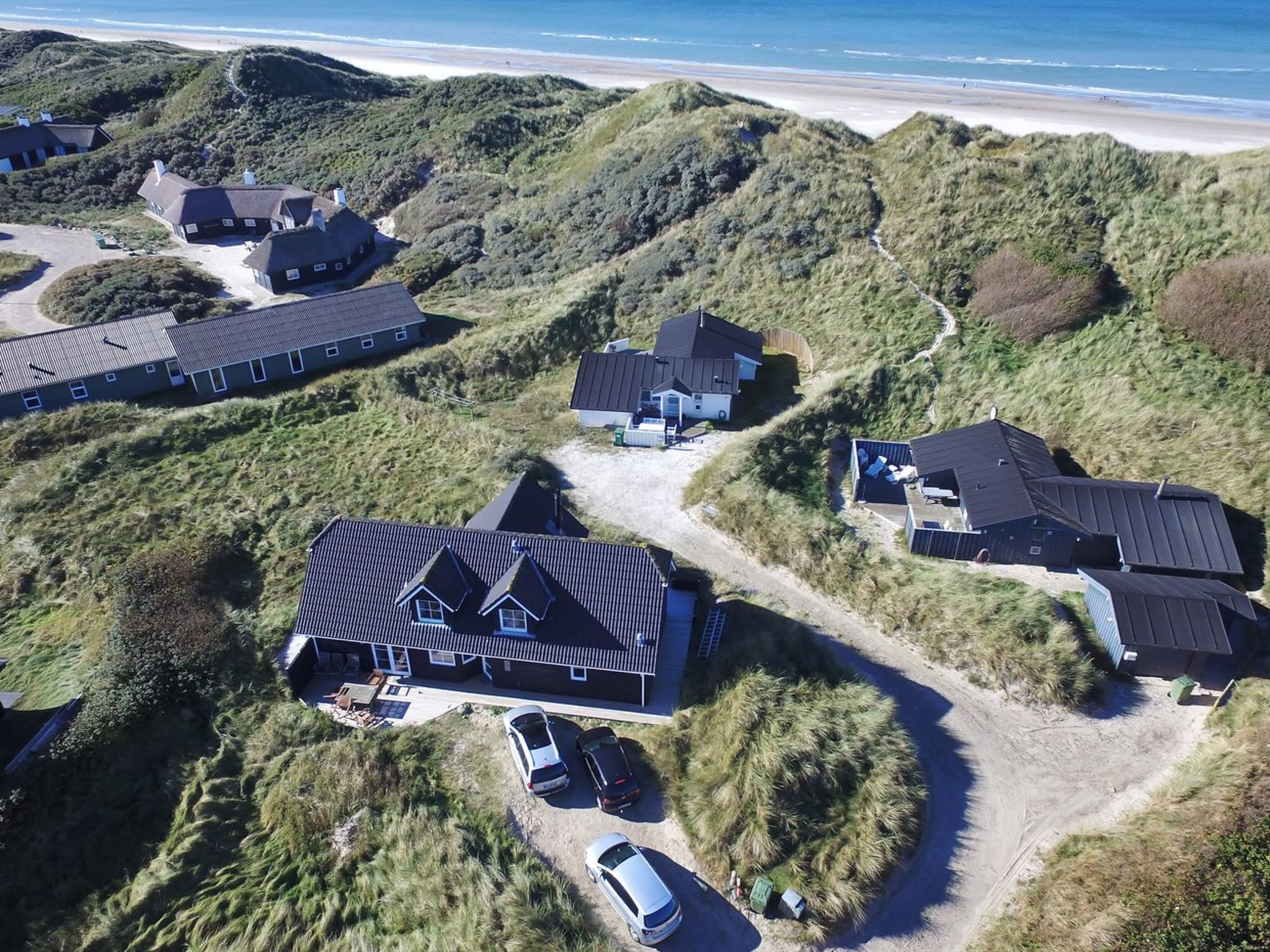 Vista aérea de una zona residencial costera con varias casas, una playa de arena y cielo despejado.