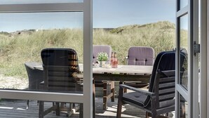 Een terras met een tafel en stoelen, met uitzicht op een strand met duinen.