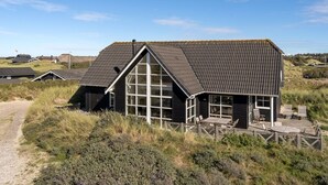 Een huis aan de kust met een groot raam, een houten terras en een grindpad ernaartoe.