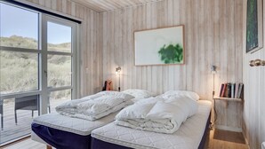 Een slaapkamer met twee bedden, houten wanden, een groot raam en een schilderij.