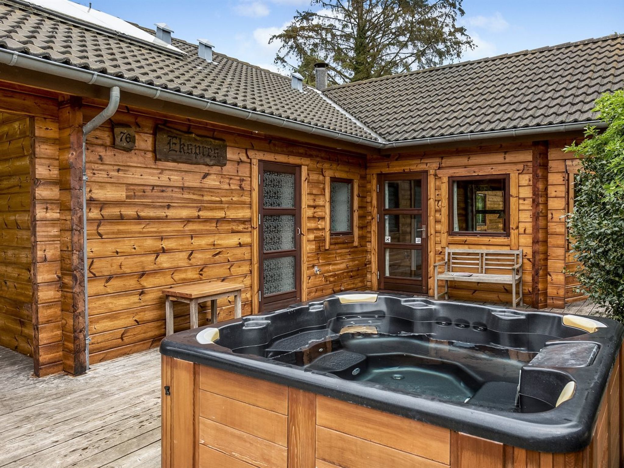 Een houten hut met een jacuzzi, een houten terras en een bankje.