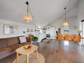 A spacious living area with a sofa, a coffee table with fruit, and a dining area with chairs and a table.