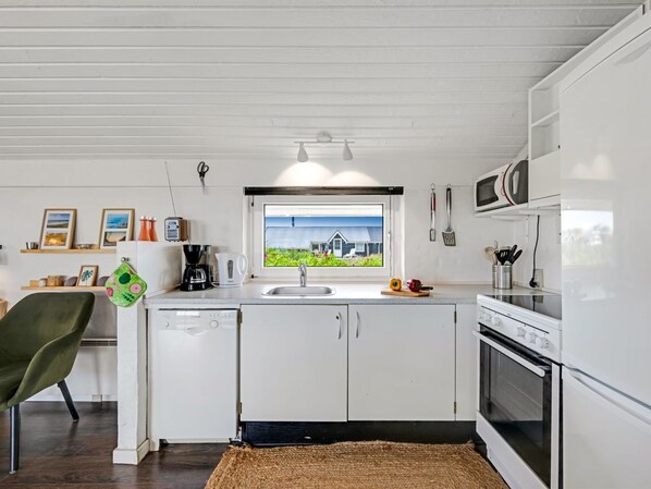 A modern kitchen with white cabinets, a built-in oven, and a window with a view of a house.