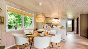 Eine moderne Küche mit Holzausstattung, ein Essbereich mit weißen Stühlen und ein großes Fenster mit Grünpflanzen im Freien.