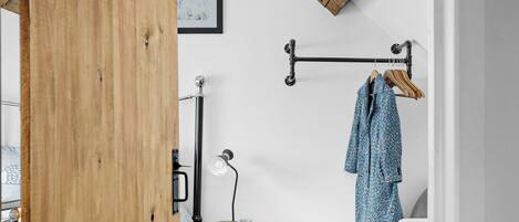 A bedroom with a wooden door, a bedside table with a lamp, a framed picture on the wall, and a coat rack with a coat.