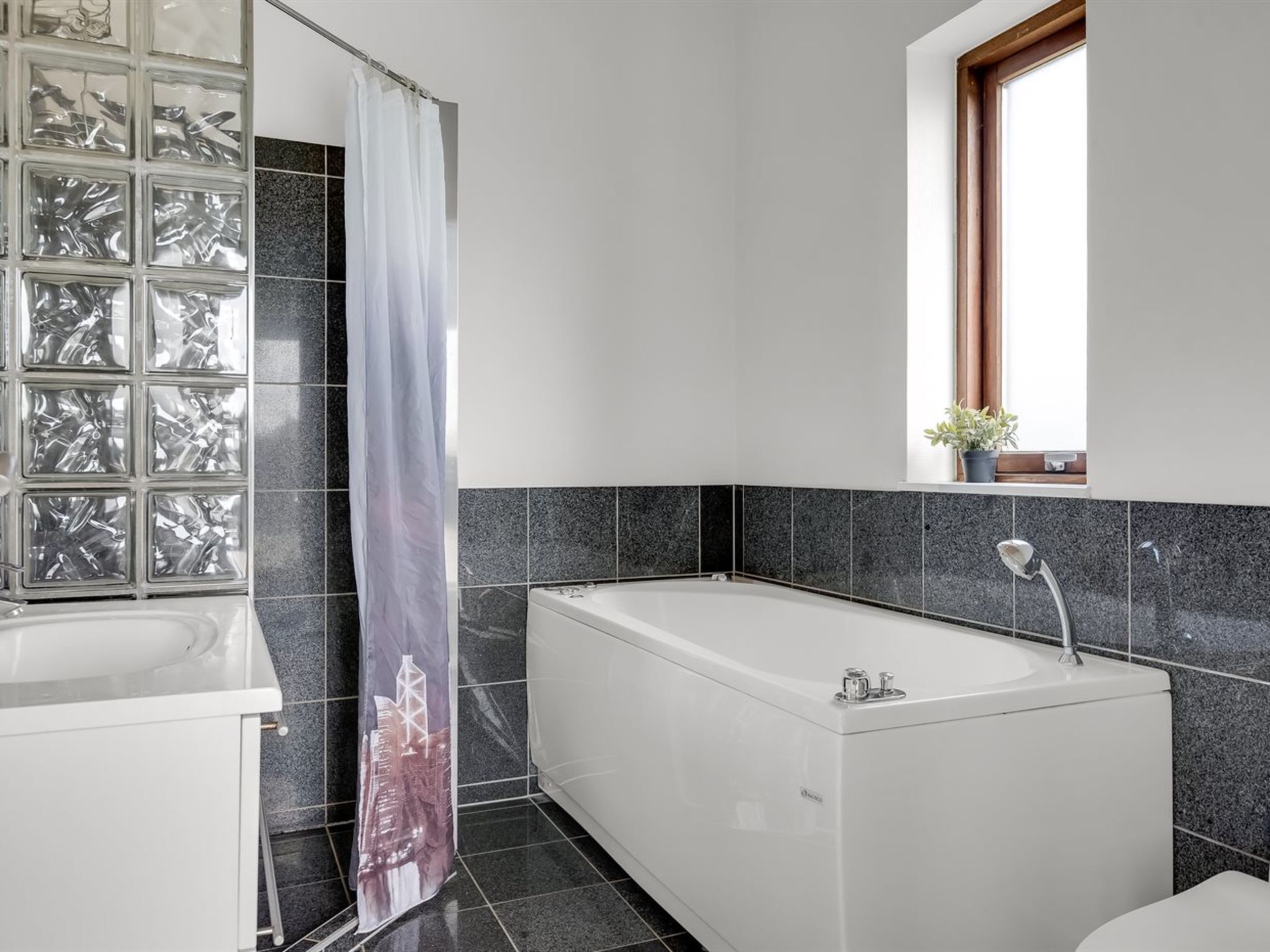 Une salle de bain moderne avec une baignoire, un rideau de douche et une fenêtre agrémentée d’une plante.