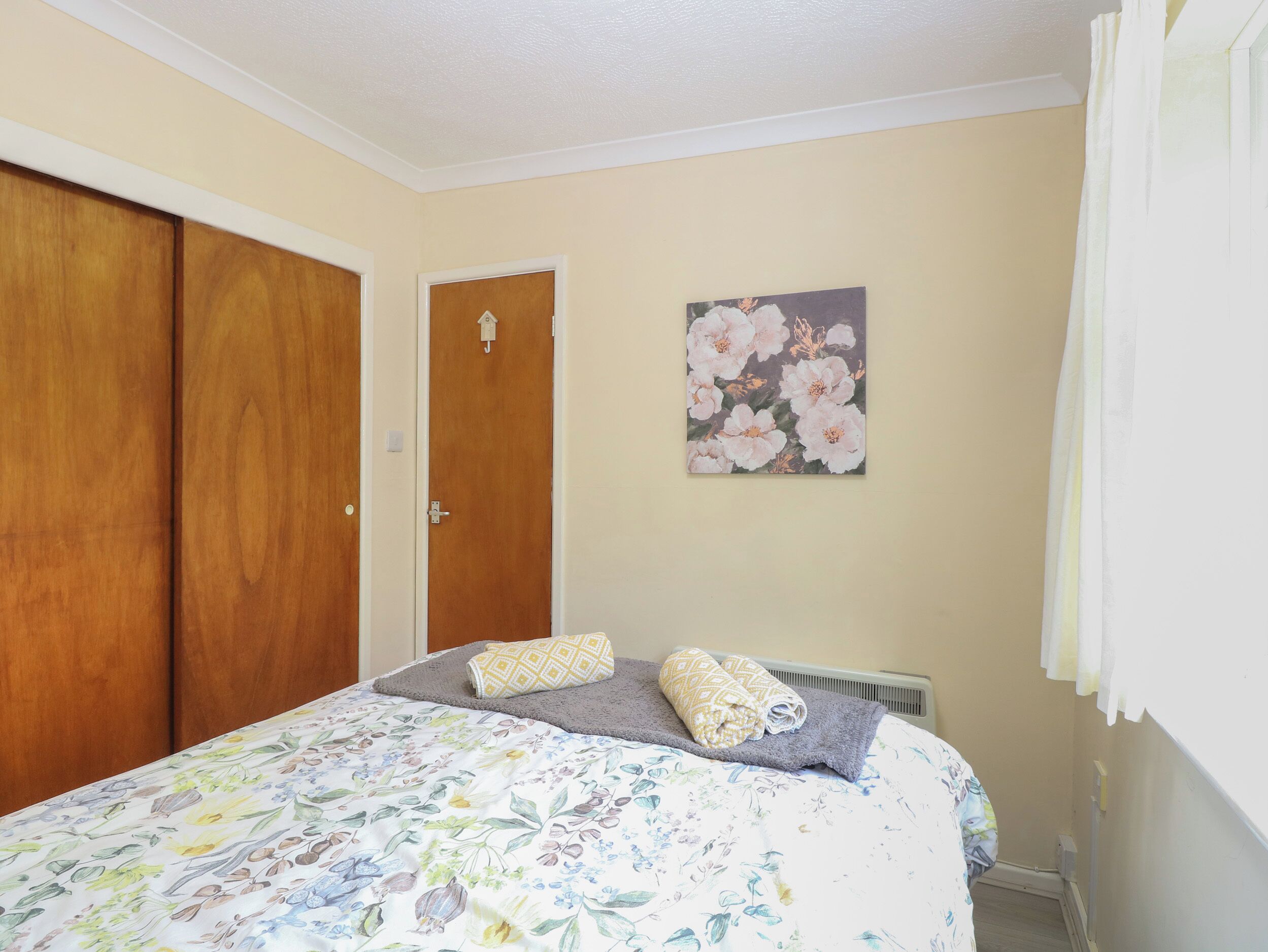 Une chambre à coucher avec une couvre-lit à motifs floraux, deux oreillers, un tableau représentant des fleurs accroché au mur et une armoire en bois.