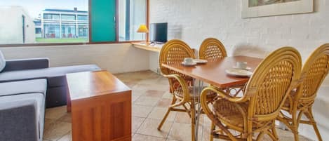 A dining area with a wooden table and wicker chairs, a sofa, and a TV on a stand.