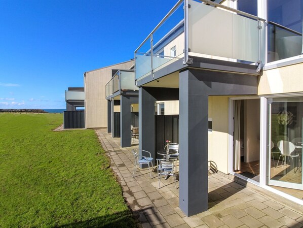 Ein modernes Haus mit Balkon, einer Terrasse mit Gartenmöbeln und Blick aufs Meer.