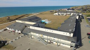 Een gebouw aan de kust met een zwembad, parkeerplaats en uitzicht op zee.