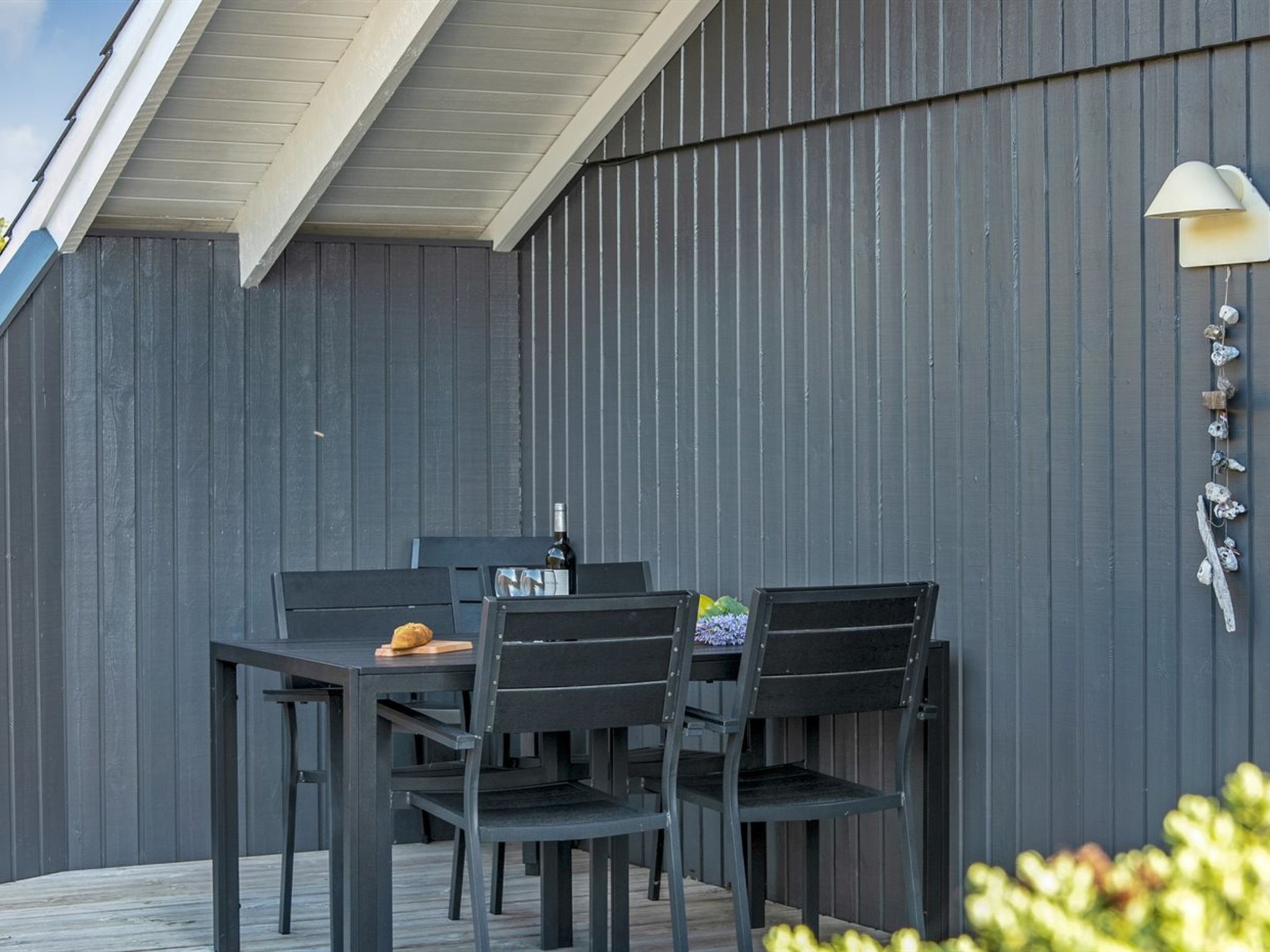 Un patio al aire libre con una mesa, sillas, una botella de vino y objetos decorativos en la pared.