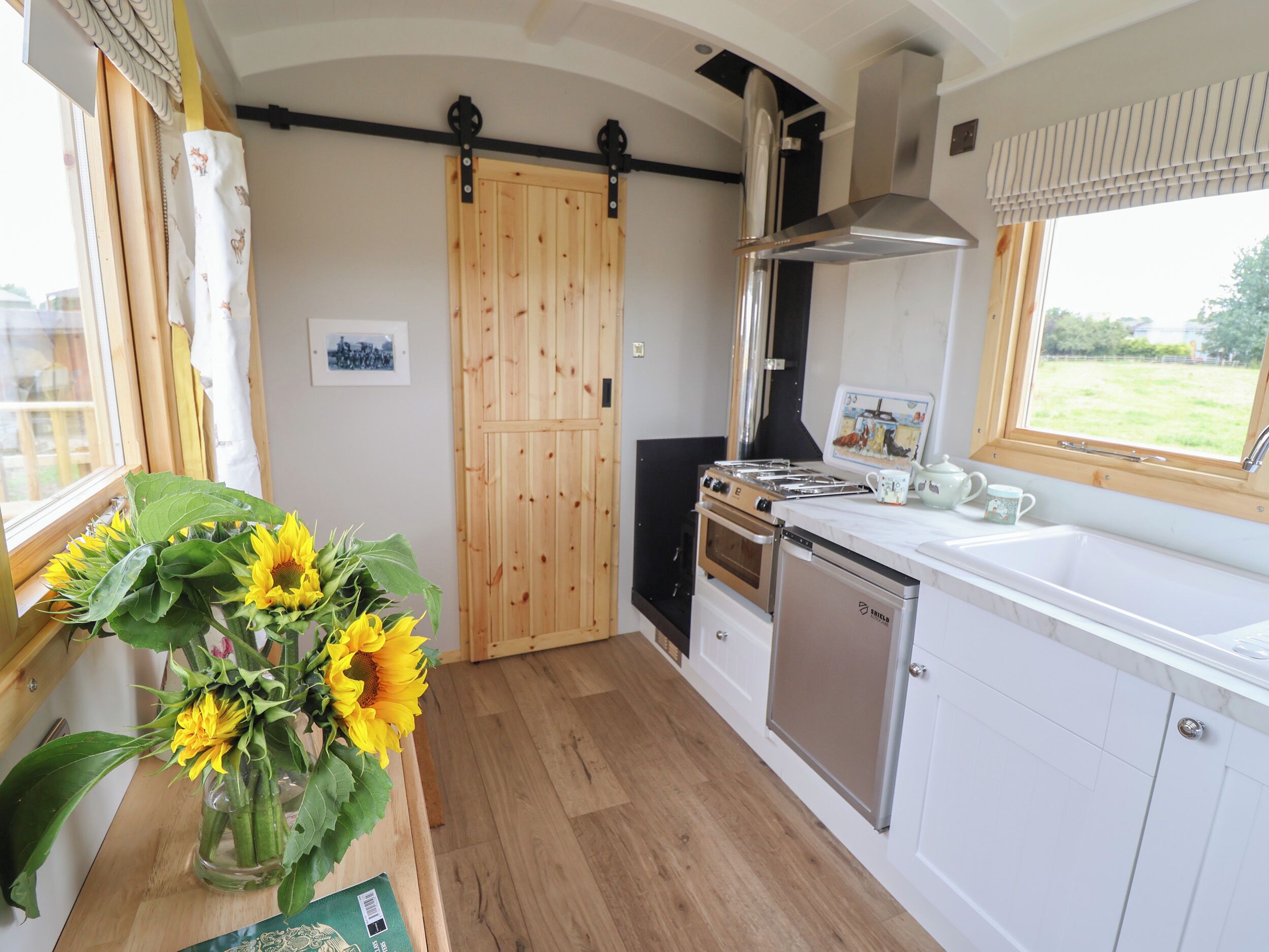 Una cocina con piso de madera, estufa a gas, campana extractora de acero inoxidable y ventana con vista al exterior.