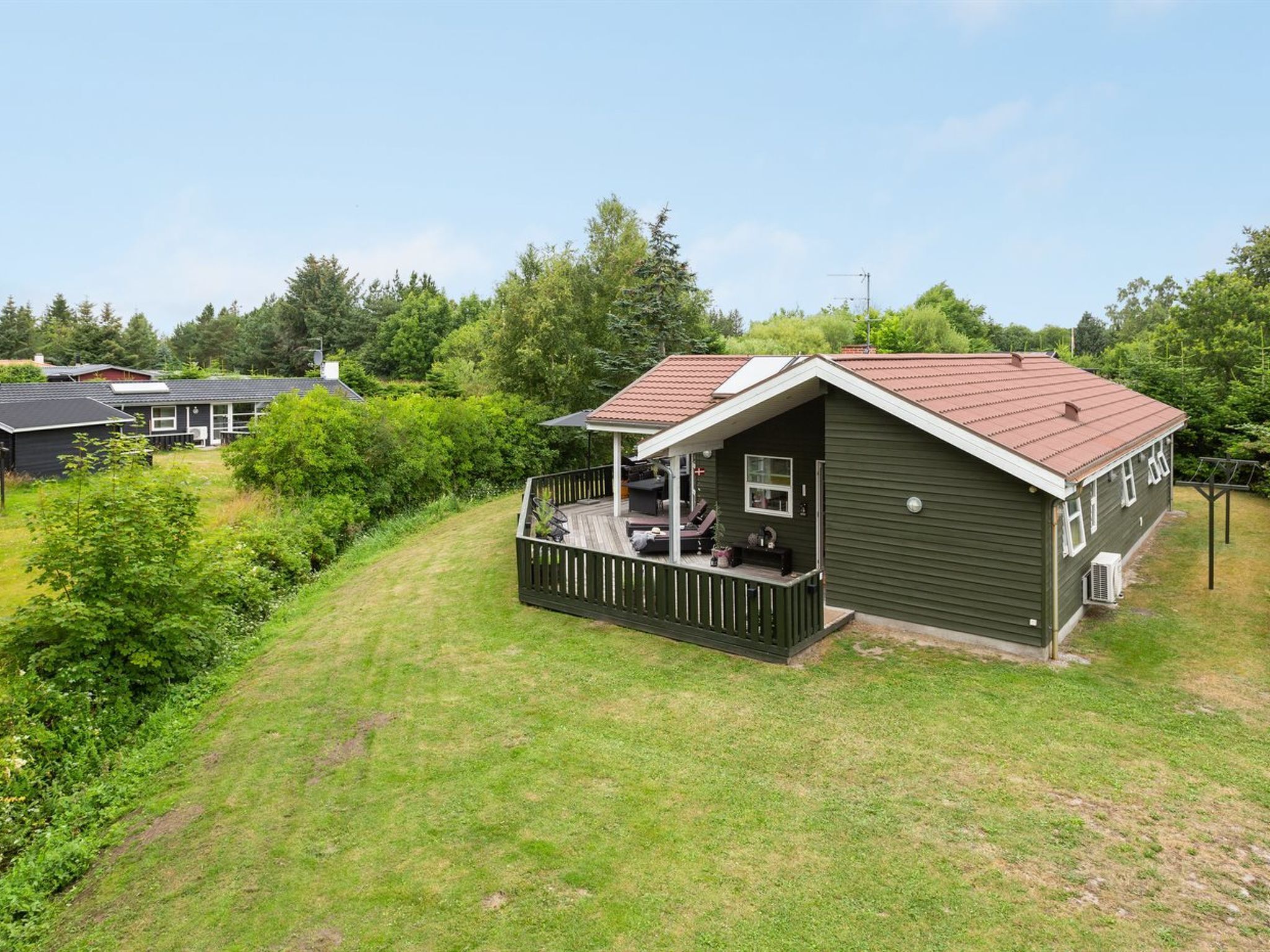 A single-story house with a porch, surrounded by a grassy yard and dense trees.