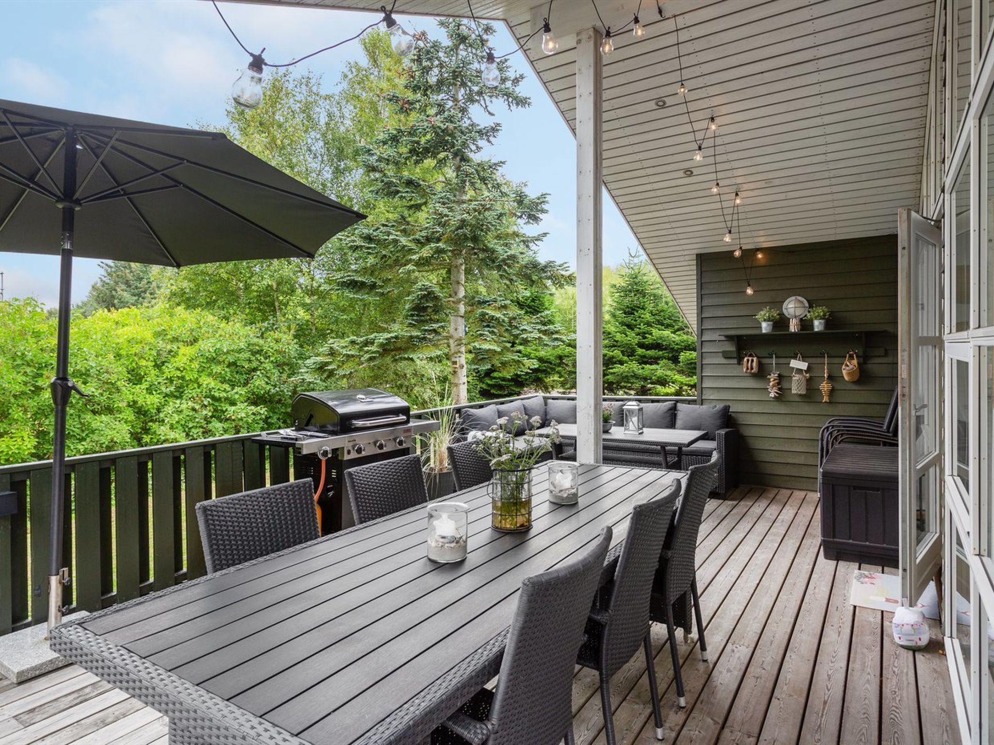 Una terraza exterior con zona de comedor, una parrilla y un área de estar con cojines.