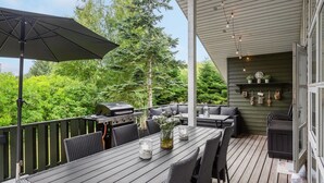 Una terraza exterior con zona de comedor, una parrilla y un área de estar con cojines.