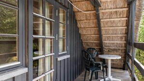 Een overdekt buitengebied met een houten terras, een ronde tafel en twee stoelen.